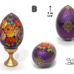 Œuf décoratif de Pâques en style russe, surface violette irisée, composition florale peinte à la main, rehaussée d’ornements dorés et d’un détail bijou, présenté sur socle, hauteur totale 12,5 cm, œuf seul 9 cm