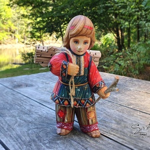 Peut inclure: Une figurine en bois d'une fille portant une robe rouge et verte, portant un fagot de bois sur le dos. Elle tient un bâton dans sa main droite. La figurine est debout sur une surface en bois. "Smal Artisanat de Collection" est écrit sur la surface.