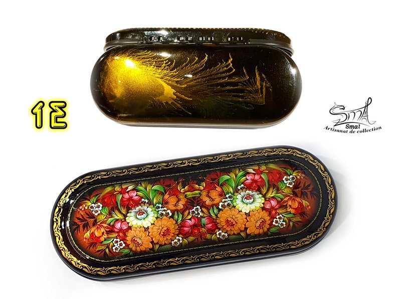 Puede incluir: Dos cajas de madera ovaladas con dise&ntilde;os intrincados. La caja superior es dorada con un dise&ntilde;o de pluma de pavo real. La caja inferior es negra con un dise&ntilde;o floral en rojo, naranja, amarillo y blanco.