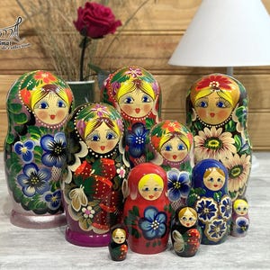 May include: A set of hand-painted Russian Matryoshka dolls. The dolls are decorated with floral and folk art designs in bright colours, including red, blue, yellow, and green. The largest doll is approximately 18 cm tall.