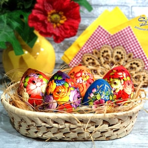 Cinq œufs de Pâques en bois peints à la main style russe dans un panier en osier. Les œufs sont décorés de motifs floraux colorés et sont disposés dans un nid de paille.