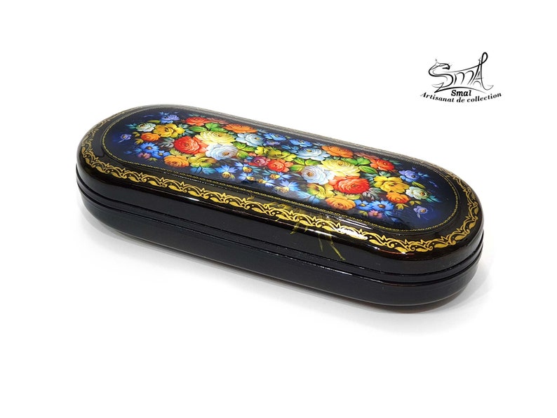 Puede incluir: Caja de madera lacada en negro con un dise&ntilde;o floral pintado en colores vivos. La caja tiene un borde dorado y est&aacute; decorada con un patr&oacute;n floral. La caja est&aacute; cerrada y se encuentra sobre una superficie blanca.