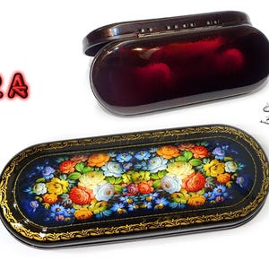Puede incluir: Una caja lacada en negro con un dise&ntilde;o floral y una tapa a juego. La caja est&aacute; decorada con un patr&oacute;n floral colorido y tiene un borde dorado. La tapa est&aacute; cerrada y tiene un peque&ntilde;o pestillo.
