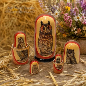 Owls hand-painted on a set of five Russian nesting dolls, featuring different owl species and detailed plumage. The Matryoshkas are arranged on a rustic wooden table surrounded by straw and dried wheat, with a colorful bouquet of wildflowers in the background, creating a warm countryside atmosphere