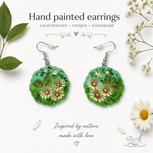 Könnte beinhalten: Handbemalte Ohrringe mit floralem Design. Die Ohrringe sind hellgrün mit weißen und gelben Blumen und grünen Blättern. Der Text "Hand painted earrings" und "Inspired by nature, made with love" ist ebenfalls sichtbar.
