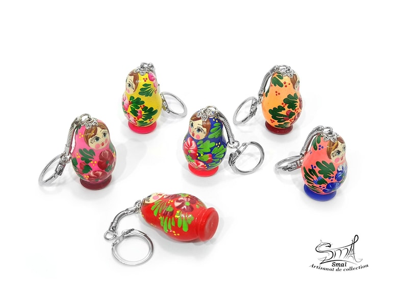 May include: A collection of colorful, hand-painted Matryoshka doll keychains. Each doll features a unique design with floral patterns and vibrant colors like red, pink, yellow, and blue. The keychains have silver-toned metal rings.