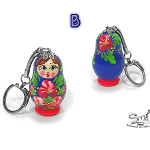 May include: Two Russian nesting doll keychains. The dolls are painted blue with red and green floral designs. Each doll has a silver-colored keychain ring attached to the top. The base of each doll is red. The text "B" is in the upper left corner.