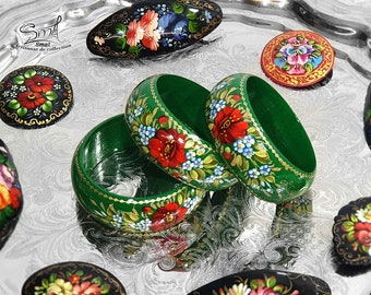 May include: Three green wooden bangles with hand-painted floral designs in red, blue, and white. The bangles are stacked on top of each other and have a gold trim.