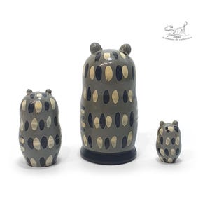 Back view of a three-piece owl matryoshka nesting doll set, showing the hand-painted gray bodies with repeating cream and dark blue feather-like patterns and glossy finish, arranged by size on a white background