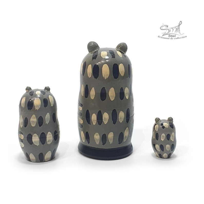 Back view of a three-piece owl matryoshka nesting doll set, showing the hand-painted gray bodies with repeating cream and dark blue feather-like patterns and glossy finish, arranged by size on a white background