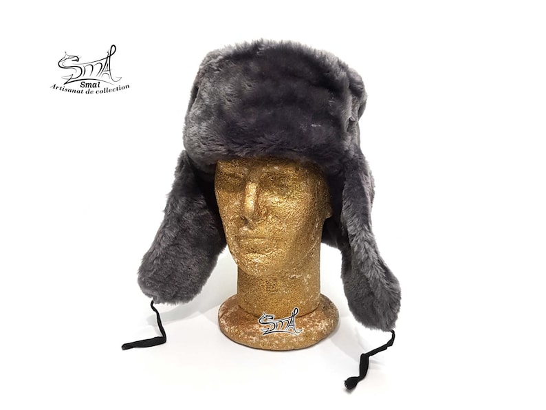 Op de afbeelding: Een grijze imitatiebont ushanka-muts met oorflappen en een zwart trekkoord. De muts zit op een mannequinhoofd.