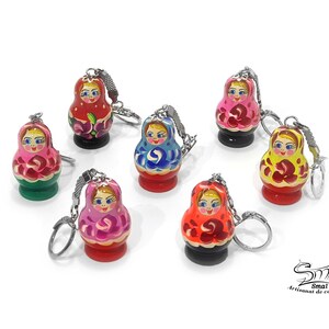 May include: Set of seven colorful wooden Russian nesting doll keychain ornaments. Each doll is painted with a different design and features a smiling face. The keychains are attached to silver rings.