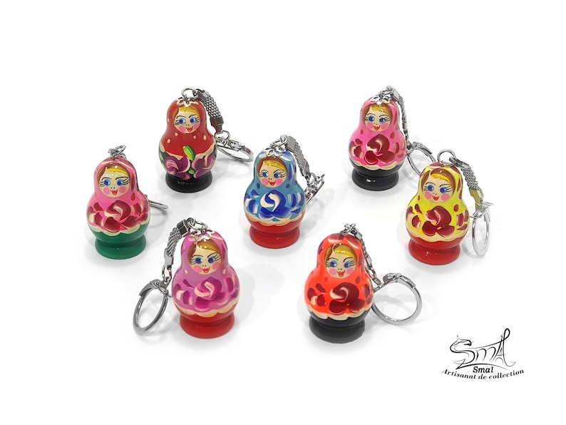 May include: Set of seven colorful wooden Russian nesting doll keychain ornaments. Each doll is painted with a different design and features a smiling face. The keychains are attached to silver rings.