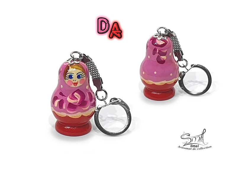 May include: A pink and red wooden nesting doll keychain with a painted face and floral design. The keychain is attached to a silver metal ring.