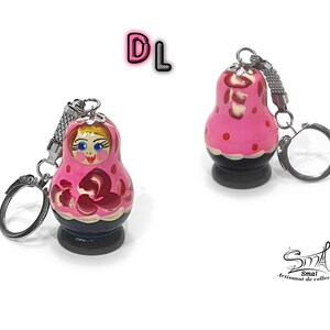 May include: Pink and red wooden nesting doll keychain with a painted face and floral design. The keychain has a silver metal ring and chain.