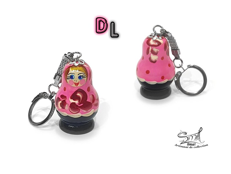 May include: Pink and red wooden nesting doll keychain with a painted face and floral design. The keychain has a silver metal ring and chain.