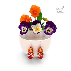 Hand-painted red Matryoshka doll earrings displayed on a white flower pot with colorful pansies, miniature Russian nesting doll dangle earrings, lightweight folk art jewelry, handmade wooden earrings by ArtSmalStudio