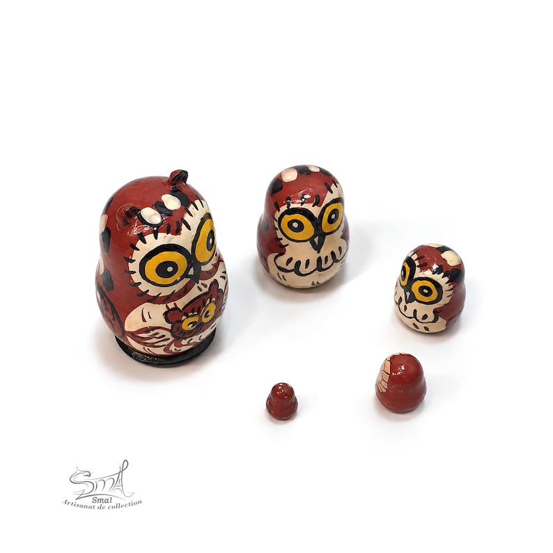 Hand-painted owl nesting doll set with five wooden matryoshka pieces, featuring charming brown and cream owls with expressive golden eyes and detailed folk-art patterns. The smallest nesting doll is shown separately, highlighting the miniature craftsmanship and compact size of this unique Russian matryoshka. A warm dark-brown and cream color palette gives the owl family a rustic handcrafted character. Displayed against a clean white background with soft natural shadows