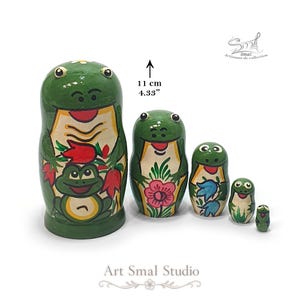 Five-piece wooden frog nesting doll set shown with the largest 11 cm (4.33") tall, featuring colorful hand-painted frog and floral designs