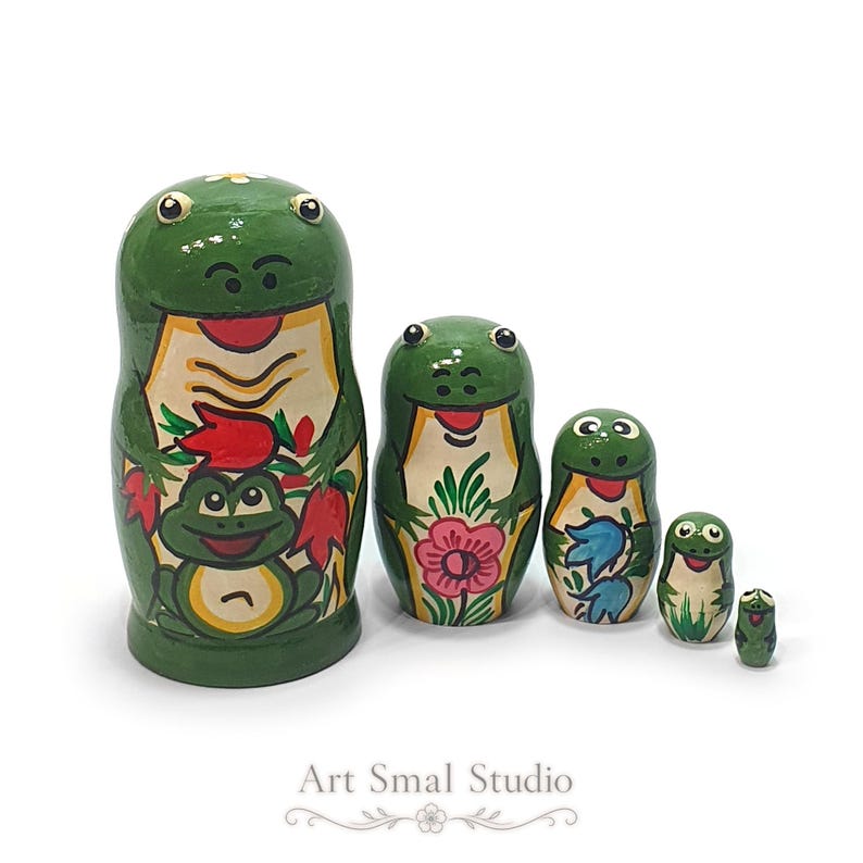 Hand-painted green frog nesting dolls, a five-piece wooden matryoshka collection displayed together on a clean white background, showing colorful frog, flower and nature motifs