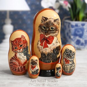 Long-haired cat hand painted on a wooden Russian nesting doll set displayed in a cozy home interior with a softly blurred background, featuring five collectible Matryoshka dolls with charming kitten portraits