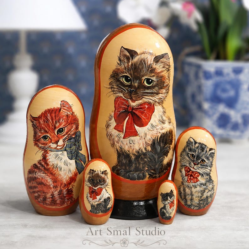 Long-haired cat hand painted on a wooden Russian nesting doll set displayed in a cozy home interior with a softly blurred background, featuring five collectible Matryoshka dolls with charming kitten portraits