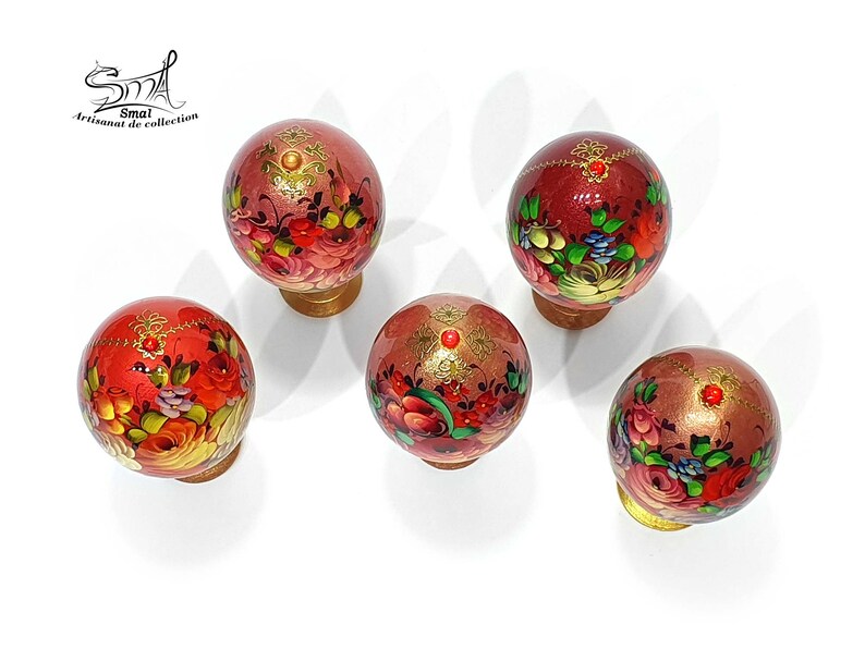 Vue de dessus d’un ensemble d’œufs de Pâques style russe, décor floral peint à la main, finition nacrée avec ornements dorés et cabochons rouges, présentés avec leurs socles décoratifs
