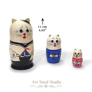 Hand-painted cat sailors featured on three Russian matryoshka nesting dolls, with each wooden doll showing a different nautical cat character. The dolls are displayed separately against a clean white background, with the largest measuring 11 cm (4.33 inches)