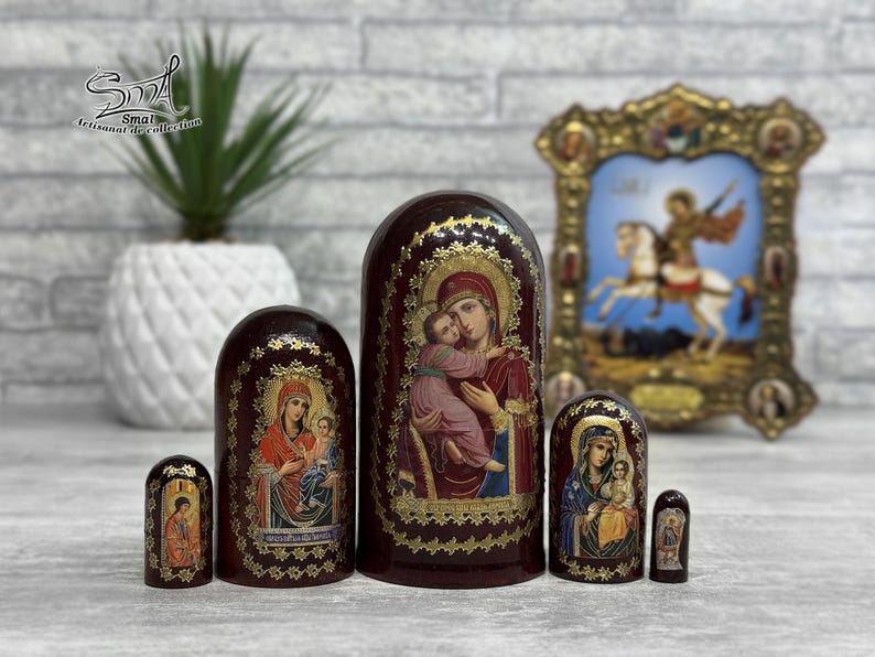 May include: A set of six Russian nesting dolls, each with a dark red base and gold accents. The dolls feature religious iconography, including images of the Virgin Mary and Jesus. A framed religious icon is in the background.