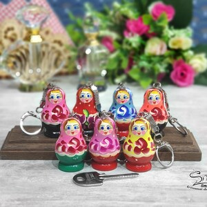 May include: A set of seven colorful wooden nesting doll keychains. Each doll is painted with a different design, including flowers, geometric patterns, and traditional Russian folk art. The keychains are attached to silver rings.