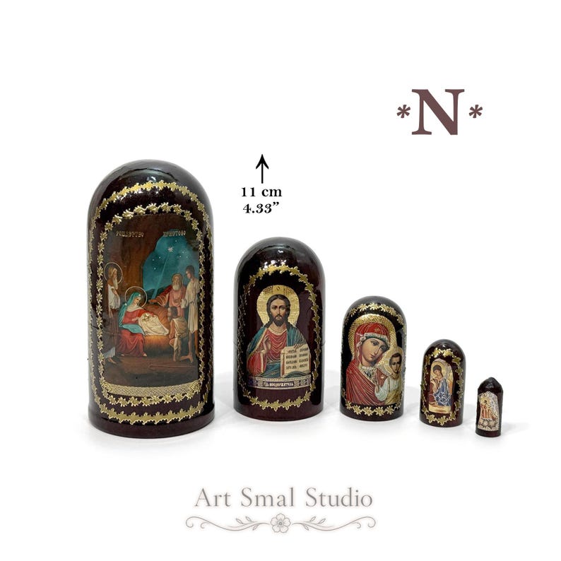 May include: A set of five dark brown nesting dolls featuring religious iconography. The largest doll measures 11 cm or 4.33 inches in height. Each piece is decorated with gold-toned floral borders and detailed paintings of biblical scenes.