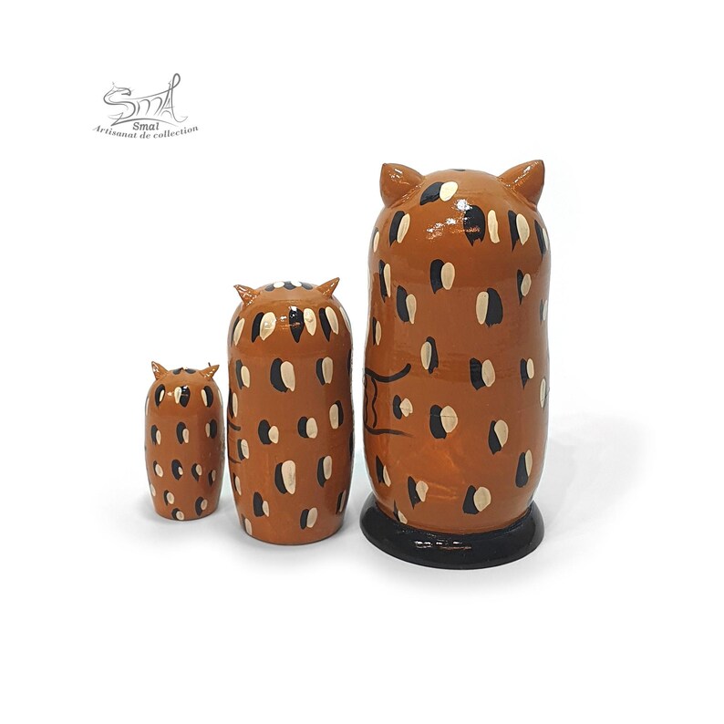 Matriochka hiboux russes en bois, 3 pièces, vue de dos, avec un motif décoratif marron, noir et beige. Les trois poupées de différentes tailles présentent des oreilles d’hibou et des détails peints à la main, avec une finition brillante