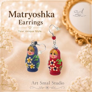 Hand-painted matryoshka doll earrings in red and royal blue. Charming Russian nesting doll dangle earrings decorated with floral folk-art patterns, rosy cheeks, blonde hair details, and delicate green leaf accents. Lightweight handmade earrings with silver-tone hooks and sparkling bead embellishments, inspired by traditional Slavic art by ArtSmalStudio