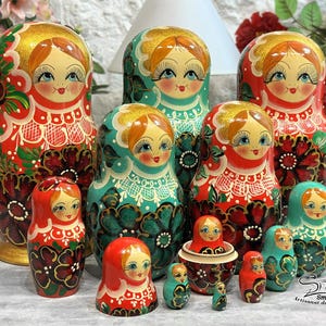 Puede incluir: Colección de muñecas rusas, o Matrioskas, de varios tamaños. Las muñecas presentan un diseño tradicional con patrones florales rojos, verdes y dorados. Las muñecas tienen caras pintadas con ojos azules y mejillas rosadas. La muñeca más grande mide unos 18 cm de alto.