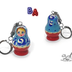 May include: A blue and red wooden keychain shaped like a traditional Russian nesting doll, or matryoshka doll. The doll has a painted face and floral designs. The keychain has a silver ring.