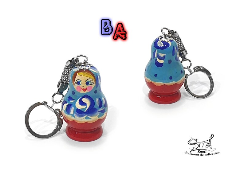 May include: A blue and red wooden keychain shaped like a traditional Russian nesting doll, or matryoshka doll. The doll has a painted face and floral designs. The keychain has a silver ring.