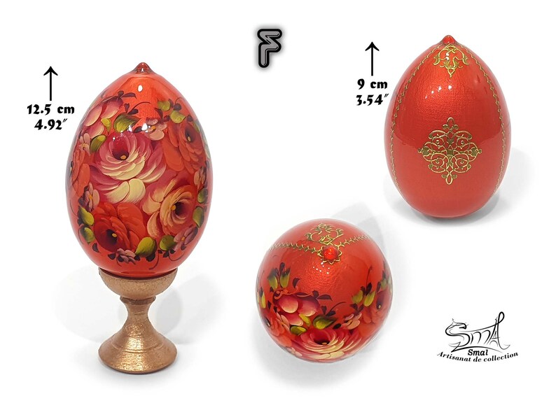 Œuf de Pâques orange intense au reflet nacré, décor floral peint à la main dans le style russe, rehaussé d’ornements dorés et d’un cabochon central, présenté avec socle, hauteur totale 12,5 cm, hauteur de l’œuf 9 cm