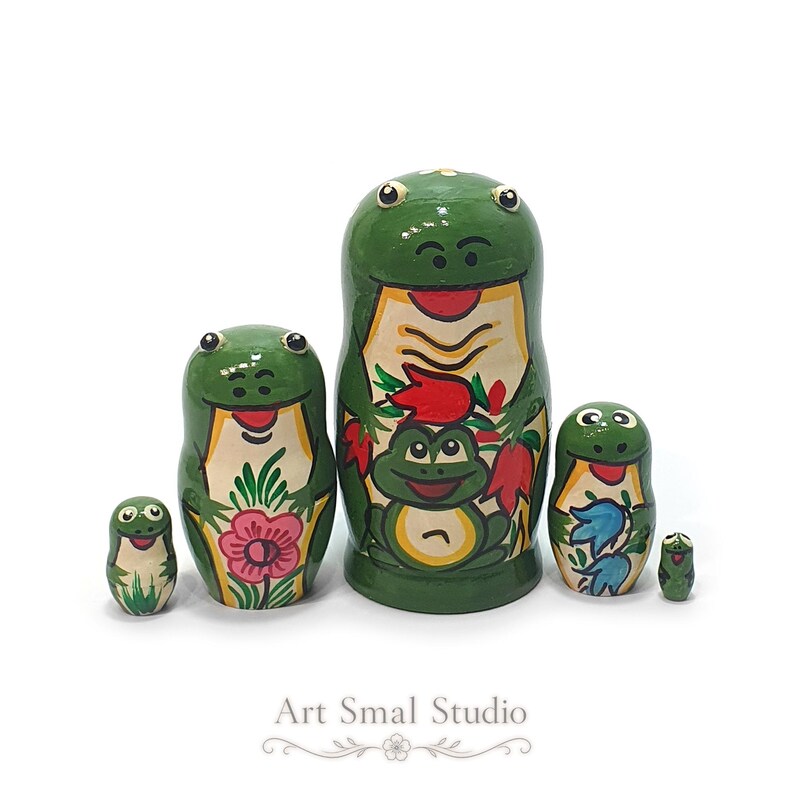 A cheerful five-piece green frog nesting doll set stands together against a clean white background, highlighting the hand-painted frog, flower and colorful nature motifs