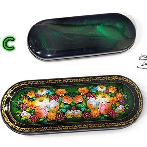 Puede incluir: Un estuche para gafas rectangular negro y verde con un dise&ntilde;o floral. El estuche est&aacute; decorado con detalles dorados y tiene un fondo negro con flores verdes y blancas.