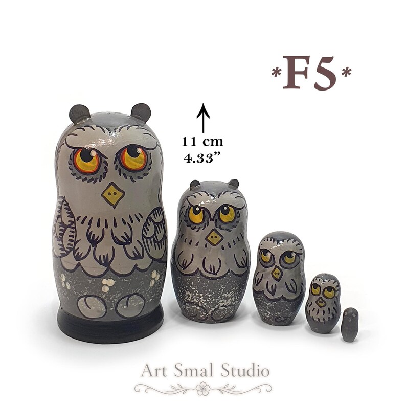 May include: A set of five nesting dolls painted as grey owls with yellow eyes and black beaks. The largest doll is 11 cm or 4.33 inches tall. The owls feature detailed feather patterns and a dark grey base. The text F5 and Art Smal Studio are visible.