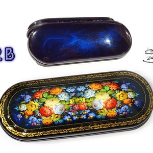 Puede incluir: Un estuche para gafas de madera lacada en azul y negro con un dise&ntilde;o floral. El estuche est&aacute; decorado con un ramo de flores de colores, incluyendo rosas, margaritas y nomeolvides. El estuche est&aacute; cerrado y tiene un borde dorado.