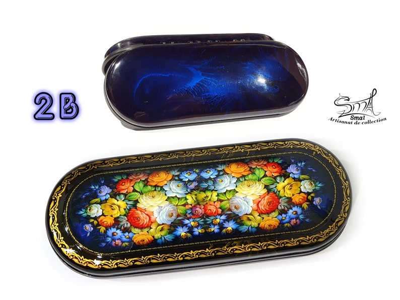 Puede incluir: Un estuche para gafas de madera lacada en azul y negro con un dise&ntilde;o floral. El estuche est&aacute; decorado con un ramo de flores de colores, incluyendo rosas, margaritas y nomeolvides. El estuche est&aacute; cerrado y tiene un borde dorado.