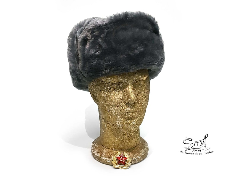 Op de afbeelding: Een grijze Ushanka-muts van imitatiebont met een rode sterspeld aan de voorkant. De muts zit op een mannequinhoofd.