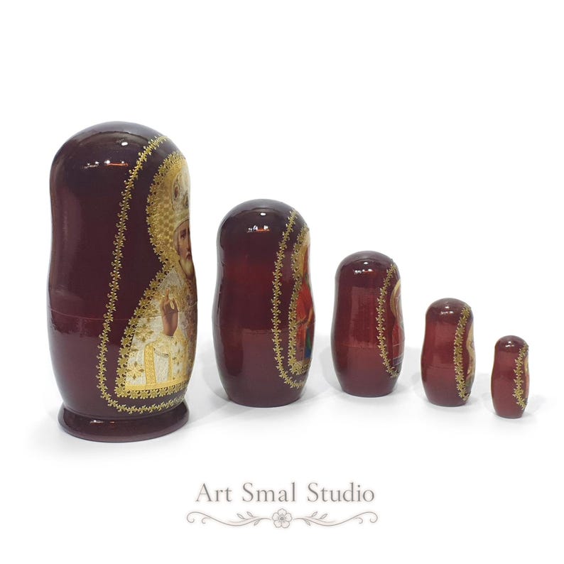Side view of a hand-painted Russian Orthodox nesting doll set of 5, showing Saint Nicholas on the largest glossy wooden Matryoshka with the remaining dolls displayed from largest to smallest.