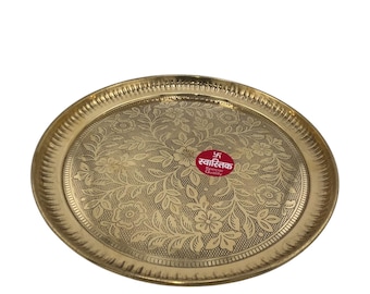 May include: A round, gold-colored metal serving tray with an intricate floral design. The tray has a raised rim and a small red sticker with the text "स्वास्तिक Special Quality" in Hindi.