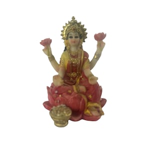 May include: A small, colorful statue of the Hindu goddess Lakshmi, sitting on a lotus flower and holding a pot of gold. She is wearing a red and gold sari and has a golden halo.