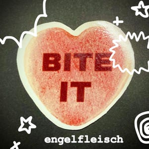 May include: A heart-shaped candy with the words "BITE IT" in red block letters. The candy is pink with a white border and the word "engelfleisch" is written below. The background is black with white doodles.