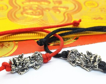 May include: Two silver dragon charm bracelets with red and black cords. The charms are detailed and have a traditional Chinese design.