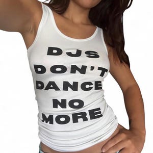 May include: White tank top with the text "DJs DON'T DANCE NO MORE" in bold black letters. The top has a scoop neckline and is made of a soft, lightweight material. A casual and comfortable top for everyday wear.