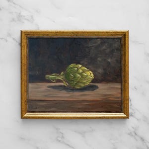 Puede incluir: Una pintura al óleo en un marco dorado que representa una alcachofa verde sobre una superficie plana frente a un fondo oscuro y sombreado. La obra presenta pinceladas visibles y una firma en la esquina inferior izquierda del lienzo.